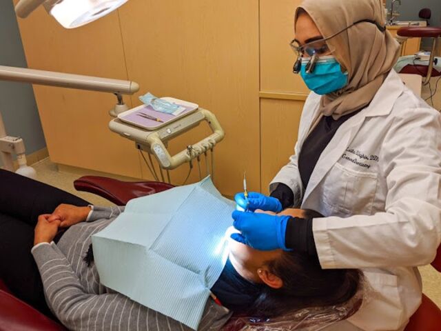 A New You Dental Center dentist, dressed in a white coat and gloves, performs a dental procedure on a patient.