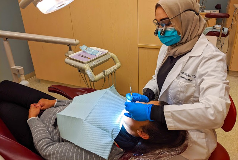 A New You Dental Center dentist, dressed in a white coat and gloves, performs a dental procedure on a patient.