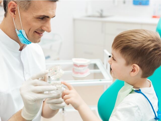 A dentist showing a young boy how to brush teeth using a dental model